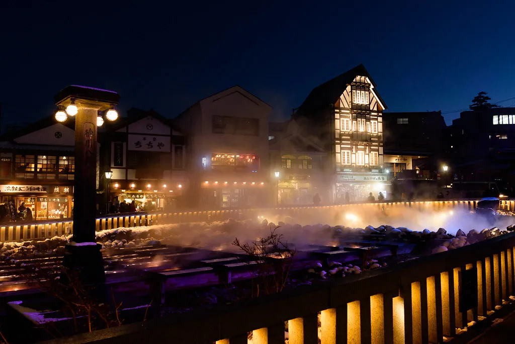 Onsen town at dusk with lanterns glowing through the steam